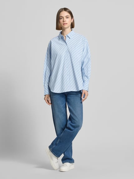 Kobiece model nosi Relaxed Fit Bluse mit Brusttasche von JJXX, bluzka z bawełny, krój relaxed fit, model JAMIE, kołnierzyk koszulowy, brustasza, długość tyłu w rozmiarze S: 78 cm, długość rękawów w rozmiarze S: 60 cm, widok całej sylwetki z przodu.