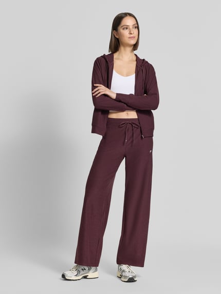 Frauenmodel trägt Wide Fit Sweatpants mit Label-Detail Modell 'CLOUD' von Fabletics, meliert, elastischer Bund, Ganzkörperansicht von vorne. Elastischer Material-Mix, Damen Sweatpants, Tunnelzug, Innenbeinlänge bei Größe S 75 cm.