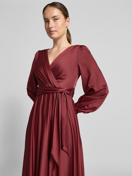 Frauenmodel trägt bordeauxrotes Tailliertes Abendkleid mit Bindegürtel von Jake*s Cocktail, weicher Stoff, Nahaufnahme Oberkörper.