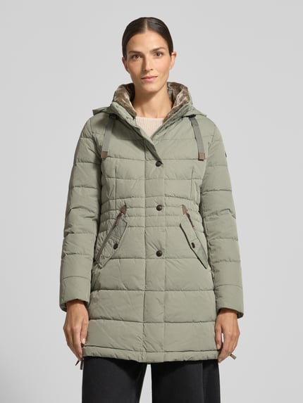 Frauenmodel trägt Steppjacke mit Kapuze von Gil Bret in Olivgrün, sichtbare Zierknöpfe, metallische Akzente, ganzkörperansicht von vorne.