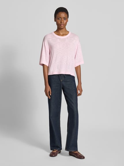 Frauenmodel trägt Relaxed Fit Pullover aus Viskose-Mix Modell 'Vicki' von FREE/QUENT in Rosa mit Rundhalsausschnitt, Stick-Optik, semitransparent, 1/2-Arm, kombiniert mit weiter Jeans, Ganzkörperansicht von vorne.