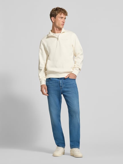 Męski model nosi Slim Straight Fit Jeans aus Baumwoll-Mix Model 'RYAN' von Tommy Jeans, denim niebieski, krój slim fit, średni stan, naszywka z logo, wyhaftowane logo, szlufki na pasek, szwy w kontrastowym kolorze, zapięcie na guzik i zamek błyskawiczny, 5 kieszeni, splot twill, mieszanka bawełny, pełny widok ciała z przodu.