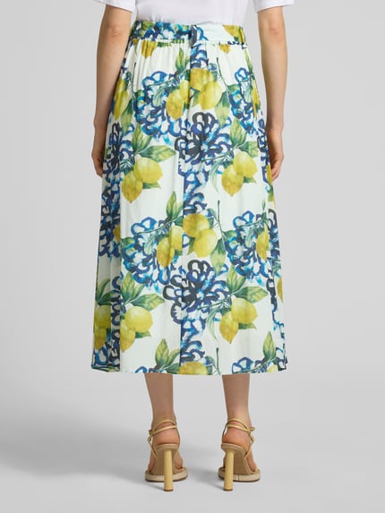 Frauenmodel trägt Regular Fit Midirock mit floralem Allover-Print von More & More, gelb-blau-grünes Muster, reine Baumwolle, Ganzkörperansicht Rückansicht.