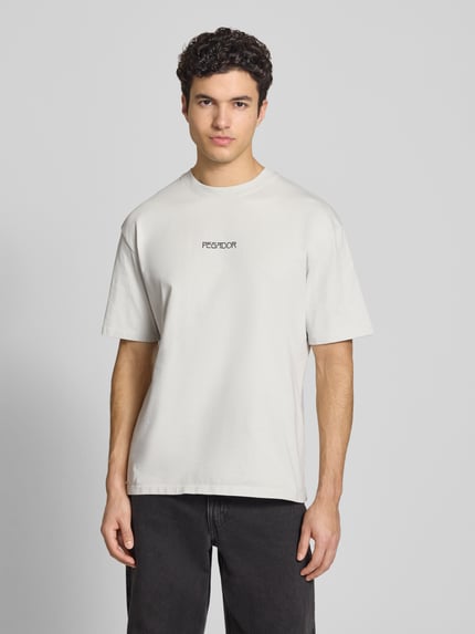 Męski model nosi Oversized T-Shirt aus Baumwolle Modell 'Stavoren' od Pegador, jasnoszary, bawełna, krój oversized fit, okrągły dekolt, detal z logo, półrękaw, długość tyłu w rozmiarze M 70 cm, widok całej sylwetki z przodu.