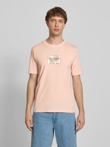 Męski model nosi T-Shirt mit Label-Print von Jack & Jones z czystej bawełny, prosty krój, jasnoróżowy kolor, okrągły dekolt, nadruk z logo, długość tyłu w rozmiarze M: 67 cm, widok całej sylwetki z przodu.
