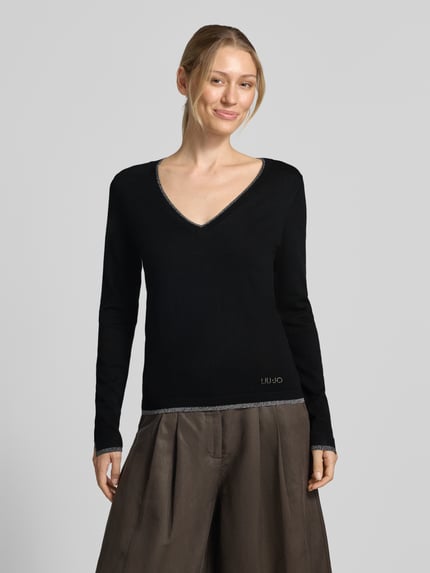 Frauenmodel trägt Slim Fit Longsleeve aus reine Viskose Modell 'Maglia Chiusa' von Liu Jo White, V-Ausschnitt, Logo-Detail, schwarze Farbe, Ganzkörperansicht von vorne.