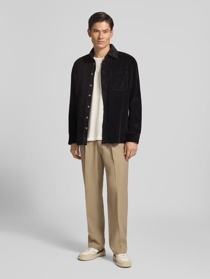 Männermodel trägt Regular Fit Hemdjacke aus Cord mit Kentkragen von Christian Berg Men in Schwarz, kombiniert mit heller Hose, Ganzkörperansicht von vorne.