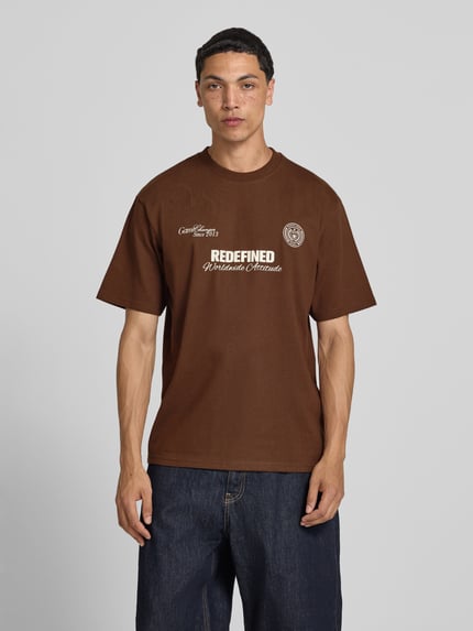 Männermodel trägt braunes Herren T-Shirt mit Statement-Print und Rundhalsausschnitt von Redefined Rebel, Baumwoll-Mix, Relaxed-Fit, Modell 'Bruno', Rückenlänge bei Größe M: 70 cm, Ganzkörperansicht von vorne.