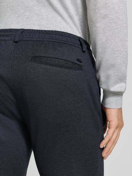 Männermodel trägt Tapered Fit Jogpants mit Viskose-Anteil Modell 'Phil' von Brax in dunklem Blau, Herren Weite Hose, Nahaufnahme Rückansicht.