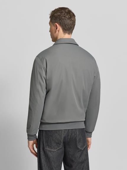 Męski model nosi szarą Jacke mit Reißverschluss von MCNEAL, regular fit, kentkołnierz, zakończenia ściągaczem, widok całej sylwetki z tyłu.