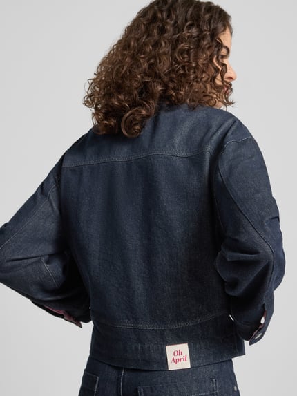 Frauenmodel trägt Regular Fit Jeansjacke mit aufgesetzten Taschen Modell 'Clara' von OH APRIL in dunklem Denim, Rückenansicht, reine Baumwolle, sichtbare Nähte, strukturierte Textur