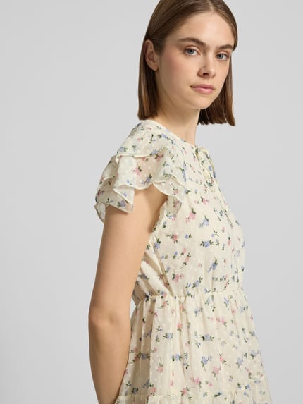 Vrouwenmodel draagt vrijetijdsjurk met all-over bloemenmotief, minilengte, ronde hals, volants, kreukdesign, model 'ELIZA' van Only, detailopname bovenlichaam.