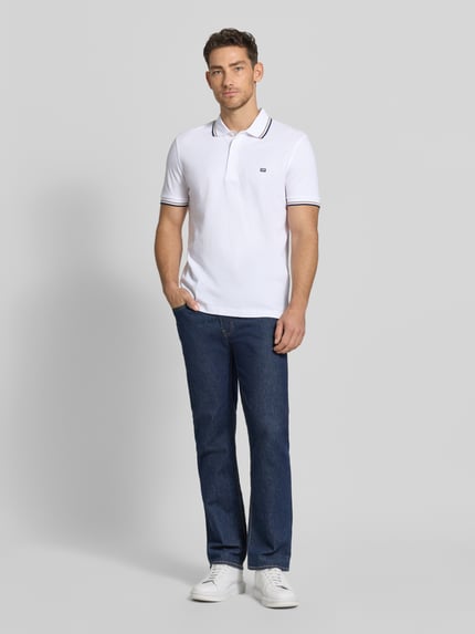 Męski model nosi Regular Fit Poloshirt mit Kontraststreifen od Christian Berg Men, biała bawełna, krój regular fit, guziki, widok całej sylwetki z przodu.