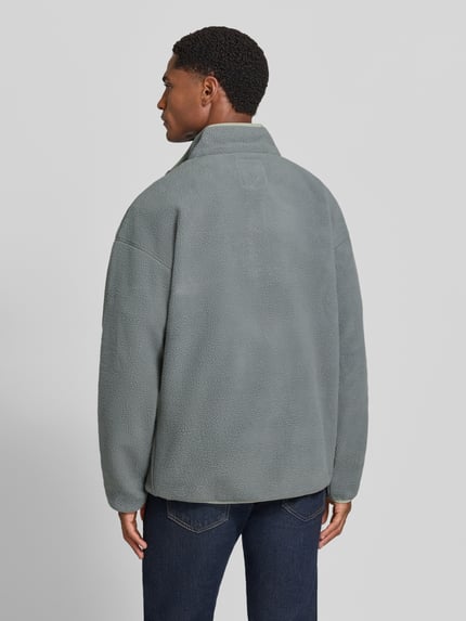 Männermodel trägt Fleecepullover mit Label-Patch Modell 'Helvetia™ II' von Columbia in Grau, strukturierte Oberfläche, Ganzkörperansicht Rückansicht. Rückenlänge 70 cm, gerader Schnitt, Stehkragen, klassische Textur.