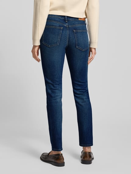 Vrouwenmodel draagt Slim Fit Jeans uit katoenmix van Tommy Hilfiger, donkerblauw, vijf zakken, logo-detail, denimtextuur. Volledige lichaamsaanzicht achterkant.