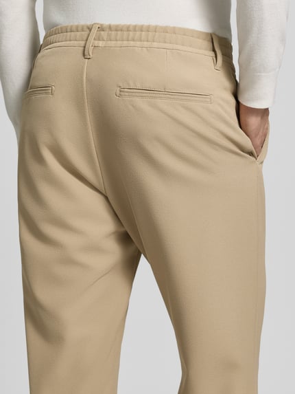 Männermodel trägt Regular Fit Bundfaltenhose mit Bügelfalten Modell 'Lui' von Strellson, beige, seitliche Eingrifftaschen, Webware, Nahaufnahme Rückansicht.