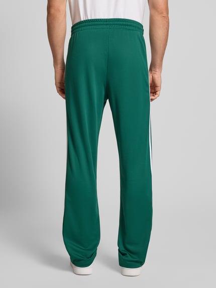 Mężczyzna nosi Sweatpants mit elastischem Bund od adidas Originals, luźny krój, zielony kolor, widoczne kieszenie, widok całej sylwetki z tyłu.