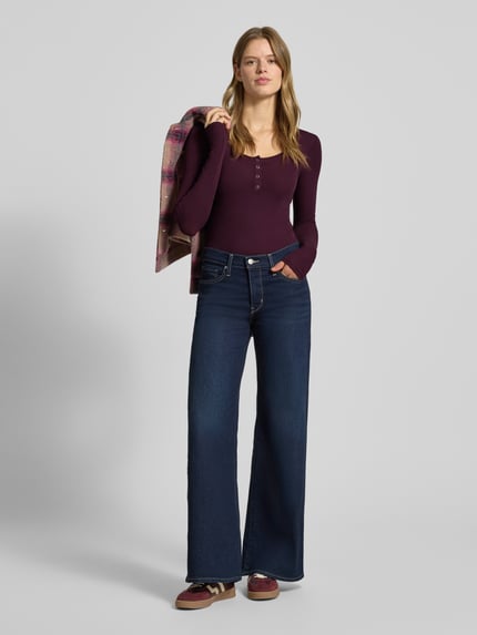 Frauenmodel trägt Slim Fit Langarmshirt aus Baumwoll-Mix Modell 'KITTE' von Pieces in unifarbener Optik mit gestreiftem Rippmuster, Henley-Ausschnitt und Druckknopfleiste, Ganzkörperansicht von vorne.
