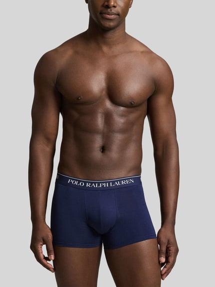 Męski model nosi obcisłe bokserki w kolorze granatowym, gładka struktura, model 'CLSSIC TRUNK-3 PACK' od Polo Ralph Lauren Underwear, z przodu cała sylwetka.