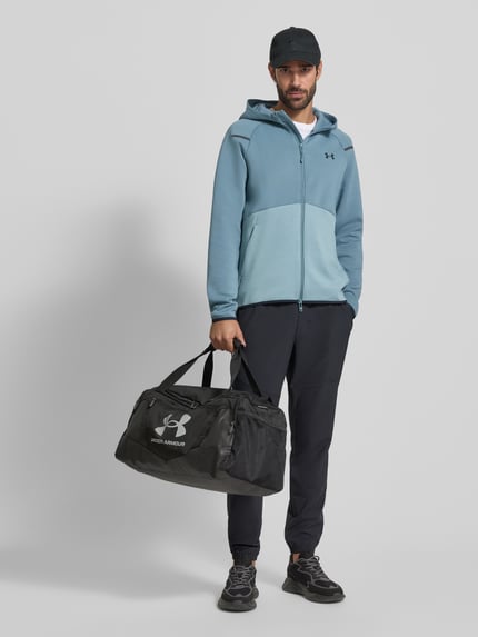 Męski model nosi Kurtka treningowa z zamkiem błyskawicznym dwustronnym Model 'Unstoppable' od Under Armour, mieszanka materiałów z dodatkiem bawełny, krój regular fit, kaptur, tył 71 cm, rękawy 60 cm, widok całej sylwetki z przodu.