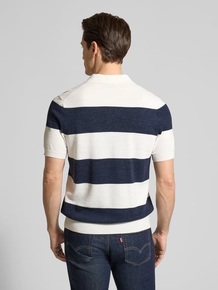 Männermodel trägt Slim Fit Poloshirt aus Baumwoll-Mix in Strick-Optik von OLYMP Level Five, breite blaue und weiße Streifen, elastische Abschlüsse, kurzärmelig, Rückenlänge 68 cm, Ganzkörperansicht Rückansicht.