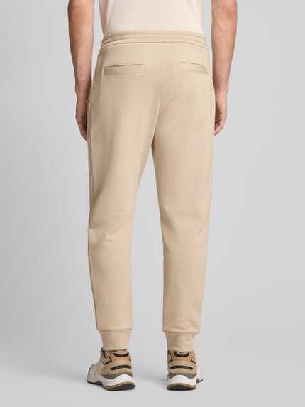 Männermodel trägt Regular Fit Sweatpants aus reiner Baumwolle von ARMANI EXCHANGE in Beige mit Gesäßtaschen, elastischen Abschlüssen, Label-Print, Ganzkörperansicht Rückansicht.