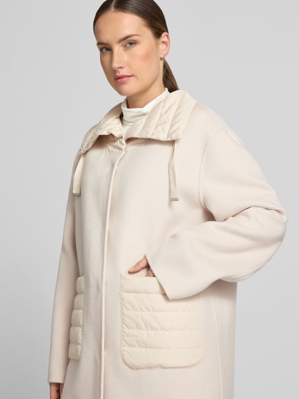 Frauenmodel trägt Mantel aus Lanawolle-Mix mit Eingrifftaschen von White Label in Creme, sichtbare Steppdetails, Nahaufnahme Oberkörper. Rückenlänge 85 cm, Schulterbreite 43 cm, Brustweite 58 cm, Ärmellänge 62 cm, gerader Schnitt, Stehkragen mit Kordelzug, verdeckter Verschluss.