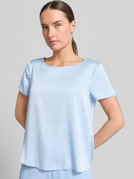 Modelka kobieca nosi Blusenshirt mit Rundhalsausschnitt und abgerundetem Saum od Rinascimento, jasnoniebieski, materiał z dodatkiem stretchu, krój loose fit, damska bluzka z zaokrąglonym dołem, długość tyłu w rozmiarze S: 52 cm, widok całej sylwetki z przodu