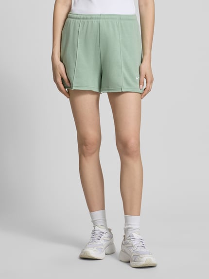 Frauenmodel trägt Regular Fit Shorts mit Tunnelzug von Nike in Mintgrün, Baumwoll-Mix, abgerundete Passform, Logo-Stitching, Ganzkörperansicht von vorne.