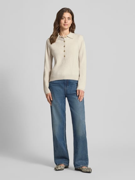 Modelka kobieca nosi Strickpullover aus Schurwoll-Kaschmir-Mix Modell 'CELLULA' von MM by Max Mara, odcień kremowy, krój regular fit, polokrage, zapięcie na guziki, długość tyłu w rozmiarze M 56 cm, długość rękawa w rozmiarze M 63 cm, tekstura miękka, styl casual, dżinsy szerokie niebieskie, buty z wzorem, pełen widok z przodu.