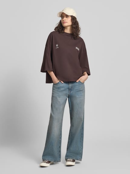 Frauenmodel trägt Oversized T-Shirt mit Rundhalsausschnitt von Karo Kauer aus reiner Baumwolle mit Label-Print, dunkelbraun, Ganzkörperansicht von vorne.