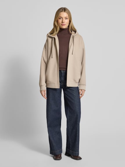 Frauenmodel trägt Oversized Sweatjacke mit Kapuze Modell 'DUNSTONE' von Drykorn im Woll-Mix, beige, grobe Textur, Ganzkörperansicht von vorne.
