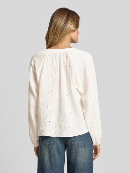 Vrouwenmodel draagt Relaxed Fit Langarmbluse aus reiner Baumwolle Modell 'NATALI' van Vero Moda in effen wit met ballonmouwen, V-hals, broderie, seersucker textuur, detailopname van achteraan.