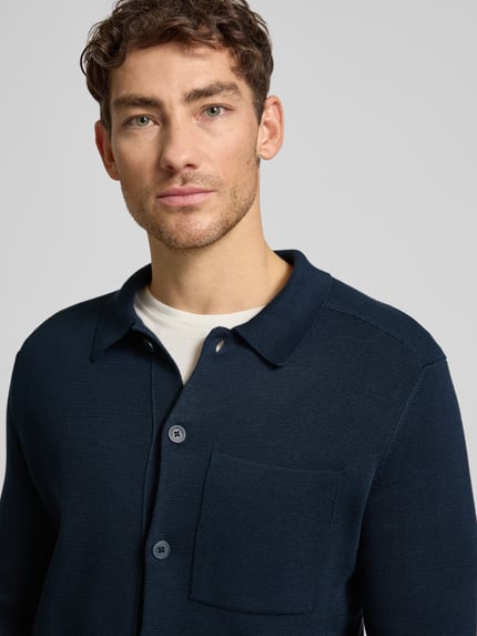 Männermodel draagt Regular Fit Strickjacke aus reiner Baumwolle van Marc O'Polo, donkerblauw, fijngebreid met borstzak, Nahaufnahme Oberkörper.