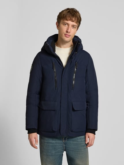 Männermodel trägt granatową Parkę mit Kapuze und kieszenie z patką od Superdry, krój regular fit, Ganzkörperansicht von vorne. Długość tyłu w rozmiarze M: 80 cm, szerokość ramion w rozmiarze M: 48 cm, szerokość klatki piersiowej w rozmiarze M: 61 cm, długość rękawów w rozmiarze M: 73 cm.