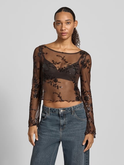 Frauenmodel trägt Langarmshirt mit ausgestelltem Ärmelabschluss von PIECES, schwarzes Mesh mit floralem Spitzenmuster, U-Boot-Ausschnitt, Ganzkörperansicht von vorne.