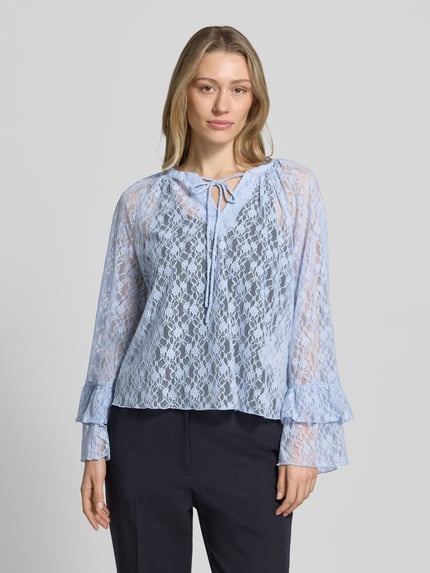 Vrouwenmodel draagt Regular Fit blouse met lange mouwen in kantlook model 'LOULOU' van Vero Moda, semi-transparante look, V-hals, striksluiting, trompetmouwen, materiaalverwerking: kant, voorkant bovenlichaam close-up.