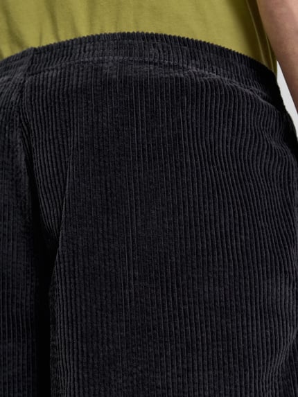 Mężczyznamodel nosi Shorts mit elastischem Bund Modell 'PADOW' von American Vintage, czarny kolor, struktura sztruksowa, loose fit z bawełny, Szerokość w rozmiarze M/L: 39 cm, długość nogawki wewnętrznej: 15 cm, zbliżenie na górną część przodu.
