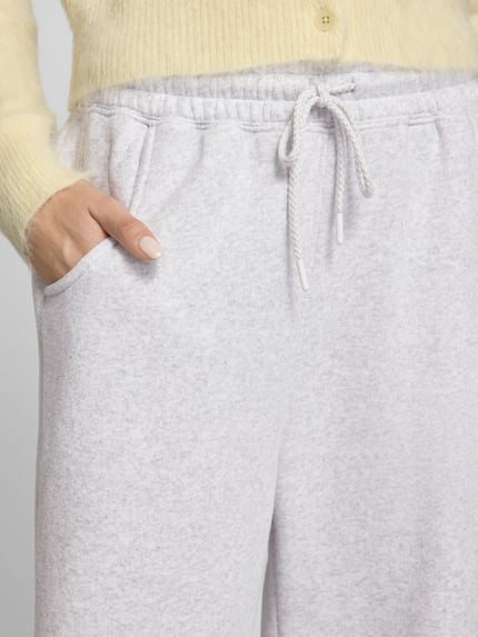 Frauenmodel trägt Sweatpants mit Baumwoll-Anteil Modell 'BAPTOWN' von American Vintage in Hellgrau mit elastischem Bund und Eingrifftaschen, Material-Mix, Nahaufnahme Oberkörper.