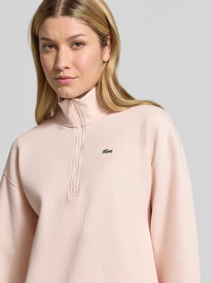 Frauenmodel trägt Relaxed Fit Troyer aus Baumwoll-Mix von Lacoste in hellem Rosa, glatte Textur, Damen Sweatshirt, Nahaufnahme Oberkörper.