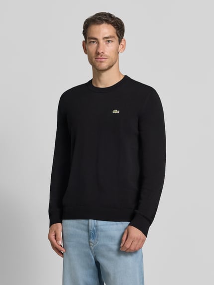Männermodel trägt schwarzen Regular Fit Pullover aus Baumwoll-Mix von Lacoste, dezentes Logo, glatte Struktur, Ganzkörperansicht von vorne. Herren Pullover von Lacoste.