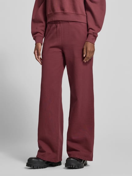 Frauenmodel trägt Regular Fit Sweathose mit Seitenschlitz von Anine Bing in einfarbigem Bordeaux, elastischer Bund, Struktur-Muster, seitliche Eingrifftaschen, Nähte, Beinabschluss mit Schlitz, Ganzkörperansicht von vorne.