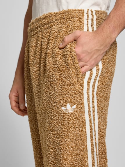Männermodel draagt Jogpants uit teddybont met labelstitching van adidas Originals, regular fit, steekzakken, elastische band, binnenbeenlengte 43 cm, detailopname rechterzij.