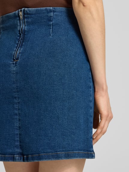 Frauenmodel trägt eng anliegenden Jeansrock aus Baumwoll-Mix Modell 'NELLY' von Vero Moda in Denim-Optik, Mini-Länge, Detailaufnahme Rückansicht.