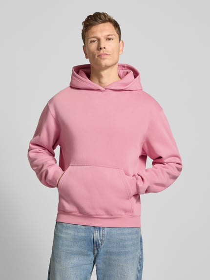 Männermodel trägt Hoodie mit Kapuze Modell 'KAMILIO' von Drykorn in Rosa, Baumwoll-Mix, lockerer Schnitt, Känguru-Tasche, Ganzkörperansicht von vorne.