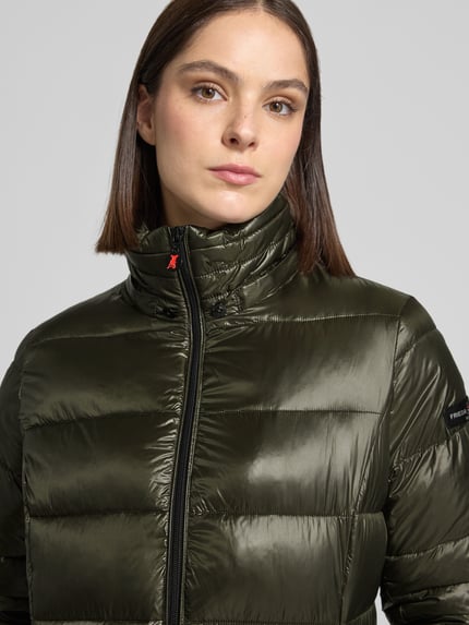 Frauenmodel trägt glänzenden, olivgrünen Puffer Coat mit Kapuze Modell 'DALIA LONG' von FRIEDA & FREDDIES, Logo-Patch, Nahaufnahme Oberkörper.