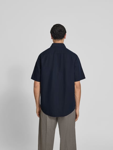 Männermodel trägt Relaxed Fit Leinenhemd mit Kentkragen van Filippa K, donkerblauw, linnenmix met katoen, korte mouw, volledige knoopsluiting, ruglengte maat 50: 81 cm, schouderbreedte: 43 cm, mouwlengte: 31 cm, relaxed fit, achteraanzicht volledige lichaamsopname.
