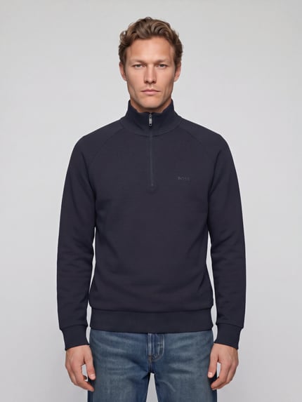 Männermodel trägt Sweatshirt mit Logo-Schriftzug Troyer von BOSS in Unifarbe mit Struktur und Reißverschluss, Ganzkörperansicht von vorne.