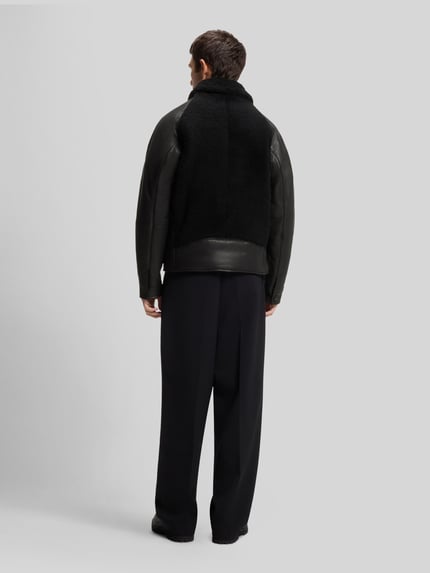 Männermodel trägt Lederjacke Modell 'Laran' mit Schnalle von HUGO in Schwarz, Regular Fit, strukturierte Optik, Glattleder und Fleece, Ganzkörperansicht Rückansicht.