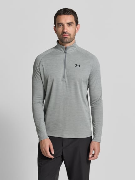 Männermodel trägt Funktionsshirt mit Logo und Reißverschluss von Under Armour in Grau, Regular Fit, Stehkragen, Ganzkörperansicht von vorne.